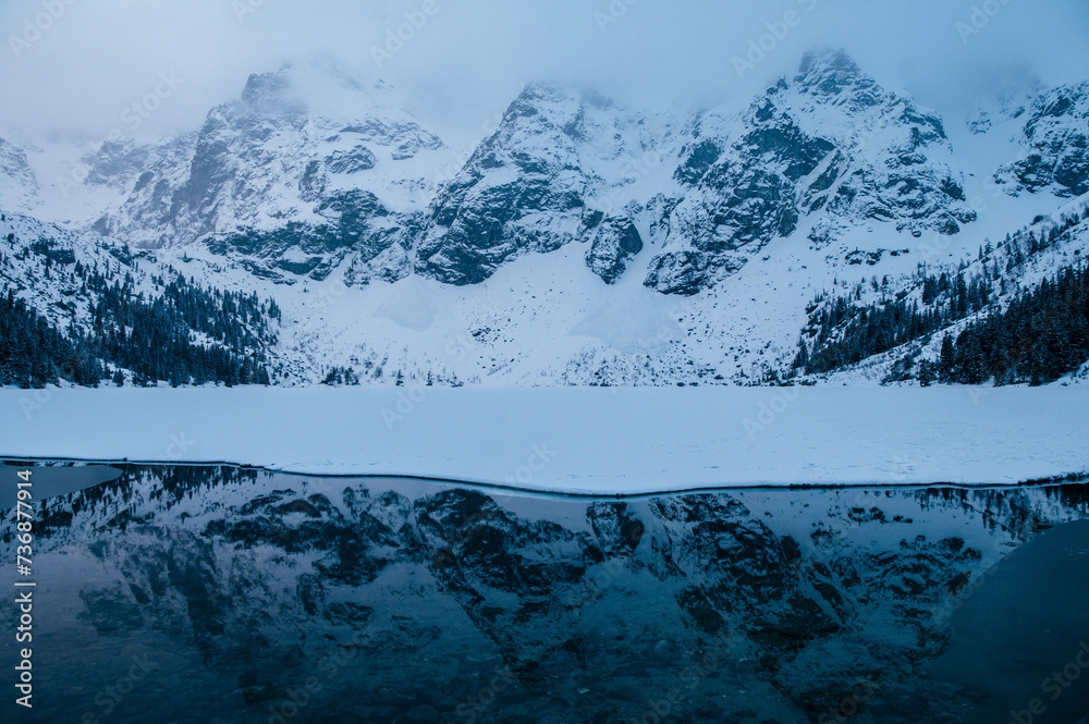 An atmospheric natural landscape with a Morskie Oko lake reflecting snowcovered mountains, creating a serene and picturesque scene with a snowy slope and ice caps. Tatry, Poland