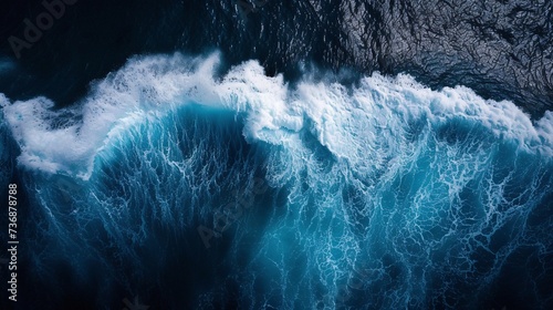 A powerful surging ocean wave is depicted in this breathtaking aerial image as it crashes into a frothy mist against the dark depths, evoking a sense of wonder and strength.