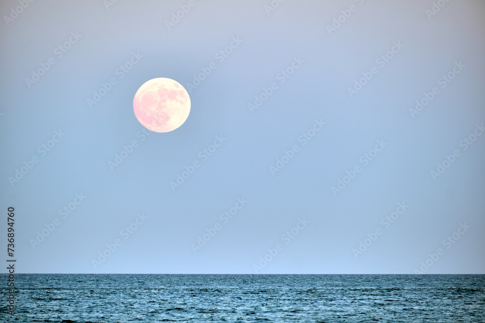 Yellow full moon hovering over the sea with clear skies