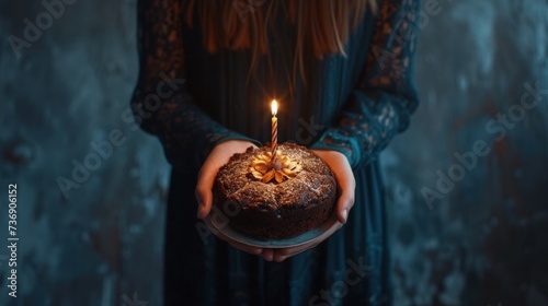 a woman holding a cake with a lit candle in it's hand with a blue wall in the background. photo