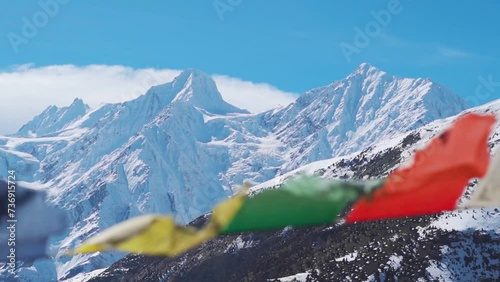 Defocused Buddhist Prayer flags waving in the wind in front of snow covered Himalayan mountains during the winter season at Keylong in Himachal Pradesh, India. Selective focus on the mountains.	