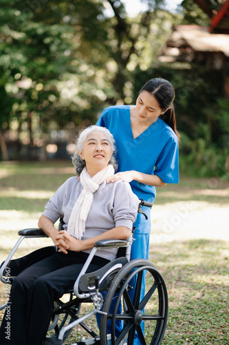 Elderly asian senior woman on wheelchair with Asian careful caregiver and encourage patient, walking in garden. with care from a caregiver and senior health insurance...