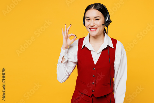 Employee fun operator business woman in set microphone headset for helpline assistance wear red vest shirt sit work at call center office show okay isolated on plain yellow background studio portrait. photo