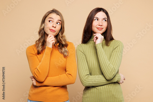 Young friend two women they wear orange green shirt casual clothes together put hand prop up on chin, lost in thought and conjectures isolated on plain pastel light beige background Lifestyle concept photo