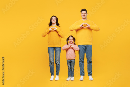 Full body young happy parents mom dad with child kid girl 7-8 years old wear pink casual clothes showing shape heart with hands heart-shape sign isolated on plain yellow background Family day concept