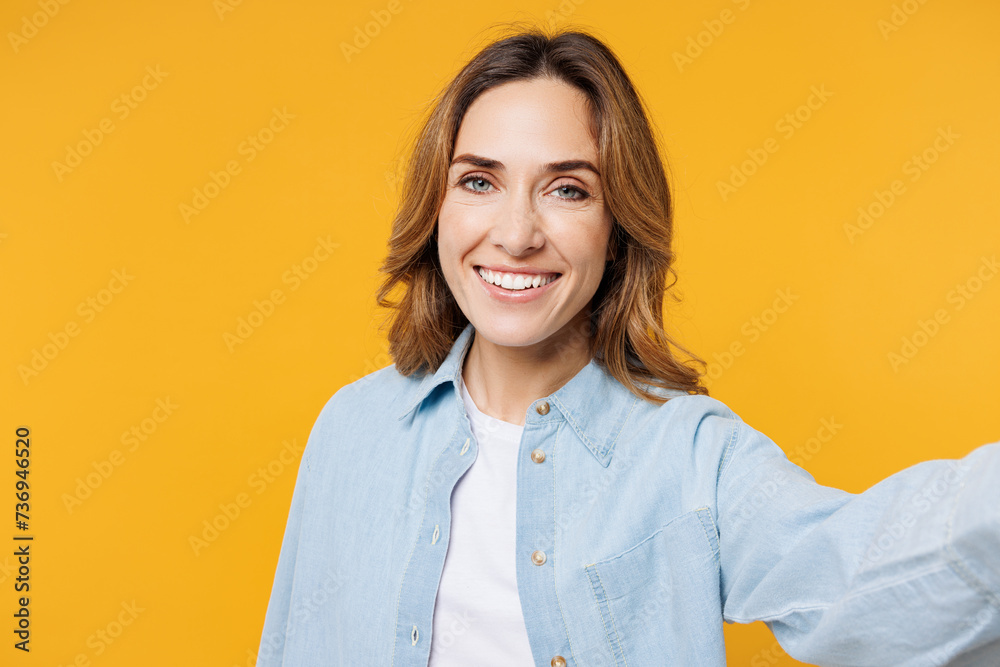 Fototapeta premium Close up young smiling happy woman she wear blue shirt white t-shirt casual clothes doing selfie shot pov on mobile cell phone isolated on plain yellow background studio portrait. Lifestyle concept.
