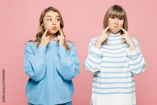 Elder cheerful parent mom 50s years old with young adult daughter two women together wear blue casual clothes point on puffed cheeks isolated on plain pastel light pink background. Family day concept. photo