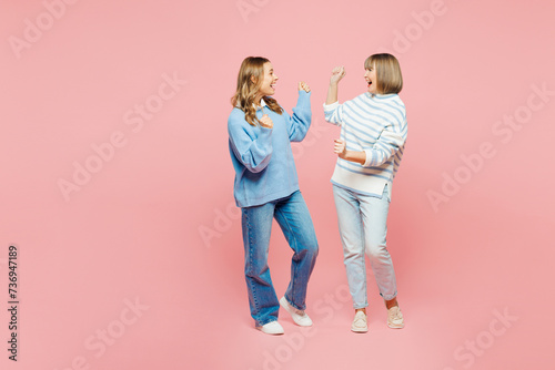 Full body elder parent mom with young adult daughter two women together wear blue casual clothes do winner gesture look to each other isolated on plain pastel light pink background Family day concept