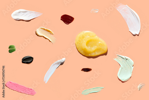 Various smears of body and face care products, including cream, butter, lotion, and scrub, on peach background under harsh sunlight. Products highlights diversity and range of skincare options