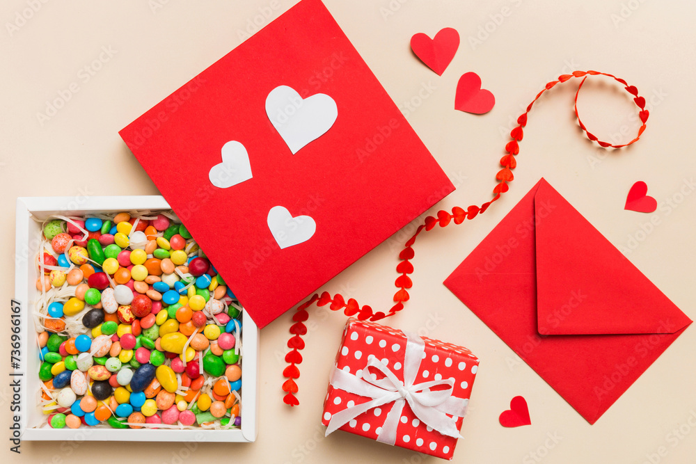 Red envelope with candy and gift box and Valentines hearts on colored background. Flat lay, top view. Romantic love letter for Holiday concept Red envelope with candy and gift box and Valentines hearts on colored background. Flat lay, top view. Romantic love letter for Holiday concept