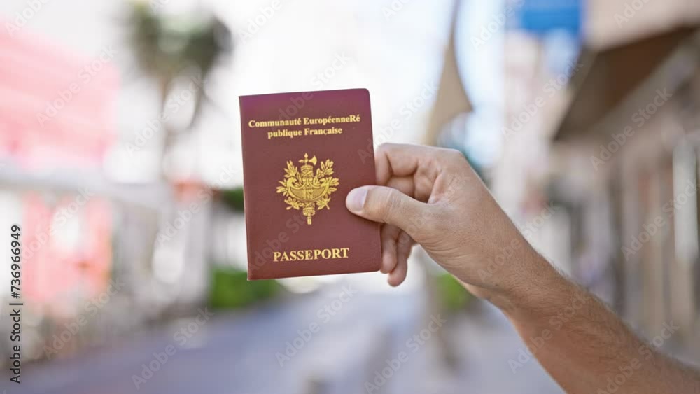 A male hand holding a french passport on a sunny urban street, exemplifying travel or immigration.