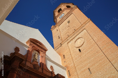 The external facade of the church of San Juan Bautista in Velez Malaga, Malaga province, Andalusia, Spain, with an impressive bell tower and a carved entrance to the church on the left