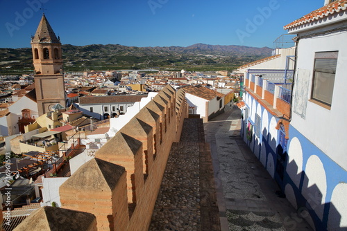 A narrow cobbled alley overlooking the town of Velez Malaga, Malaga province, Andalusia, Spain, with ramparts, whitewashed houses and the bell tower of the church of San Juan Bautista