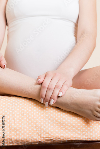 Pretty pregnant woman hands massaging leg sitting on bed