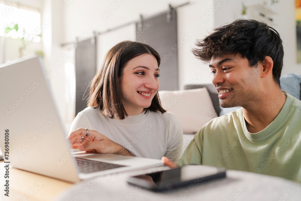 Young couple sharing a fun moment while shopping online, with the woman pointing at the laptop screen and smiling Young couple sharing a fun moment while shopping online, with the woman pointing at the laptop screen and smiling