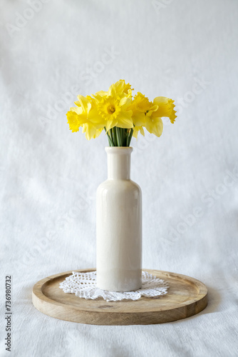 Still life with a blooming bouquet of yellow daffodils in an elegant porcelain vase on a textured white background