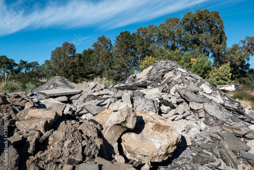 Estaleiro com pilha de aterro de restos de estrada de asfalto para reaproveitamento para enchimento de outras obras, com uma floresta com fundo num dia de céu azul photo