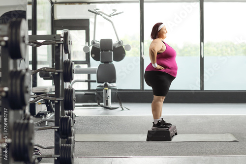 Full length profile shot of a plus size woman in sportswear standing on a stepper