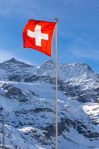 Detail of the Swiss flag waving very strongly due to the strong wind. In the background the snow-capped mountain.