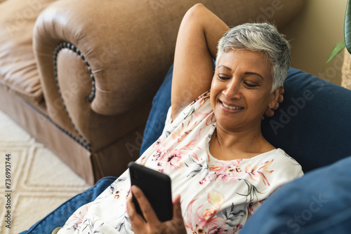A mature biracial woman appears relaxed while using her smartphone at home, with copy space photo