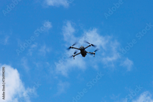 Modern quadcopter flies against the blue sky. Copy space.