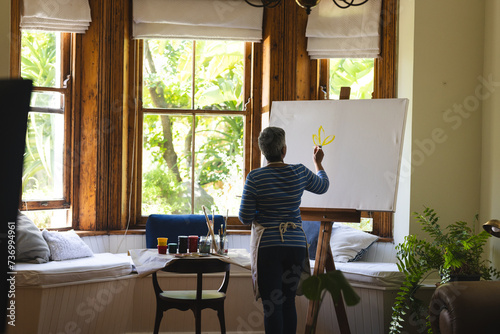 A mature biracial woman artist paints on a canvas at home, with copy space photo