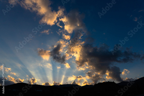 Sun light rays shining through dark clouds over mountains.