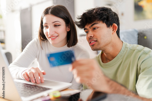 Happy couple engaged in an online purchase, with the man holding a credit card and the woman typing on a laptop photo