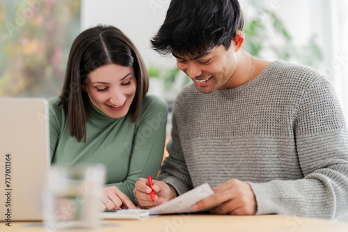 Young couple intently reviewing documents and working on a laptop at home