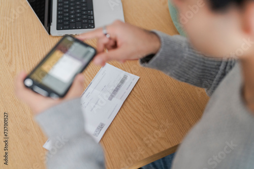 Close-up image of a smartphone in a man's hands, displaying a scanned bill on the screen. It highlights the use of mobile technology for online payment