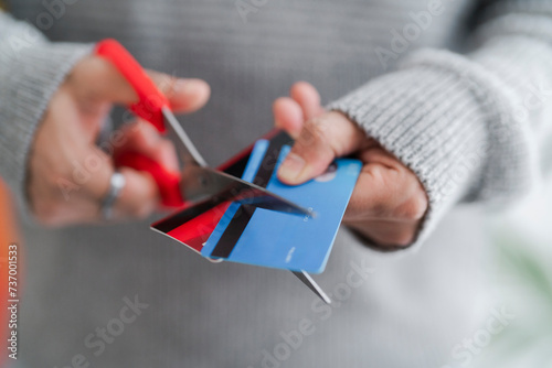 A man's hands cutting a blue credit card with red scissors, symbolizing financial management or the end of a credit account. The decisive cut reflects personal finance decisions photo
