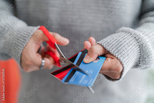 A man's hands cutting a blue credit card with red scissors, symbolizing financial management or the end of a credit account. The decisive cut reflects personal finance decisions photo