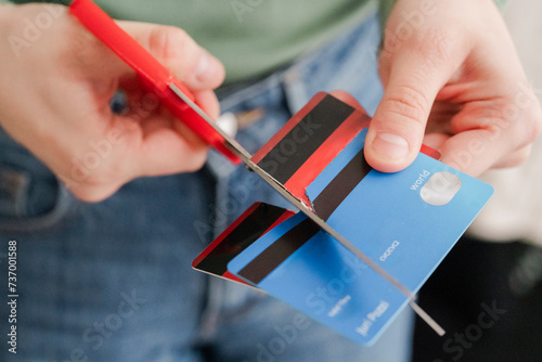 A person in a green sweater is seen cutting a stripe-patterned credit card with red scissors. The act signifies the intention to reduce debt or prevent overspending photo