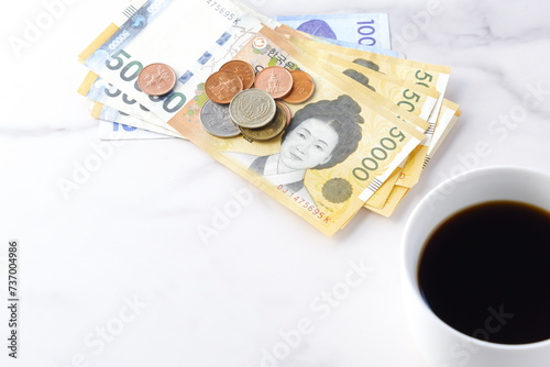 韓国の通貨、ウォンKRW（紙幣と硬貨）と、コーヒーの入ったコーヒーカップ  © theghan
