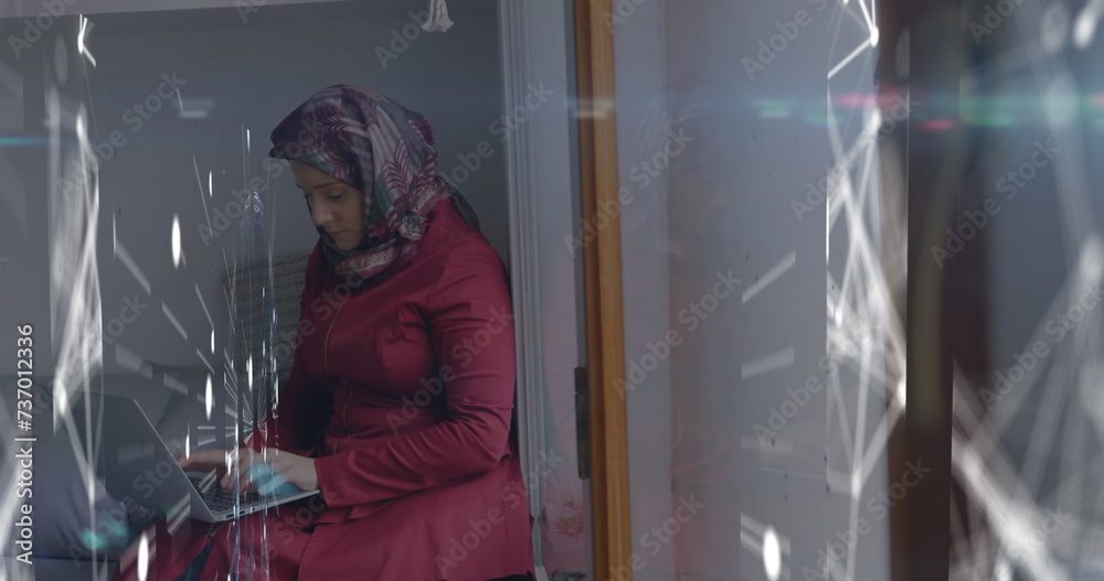 Image of digital interface with network of connections over woman in hijab using laptop computer