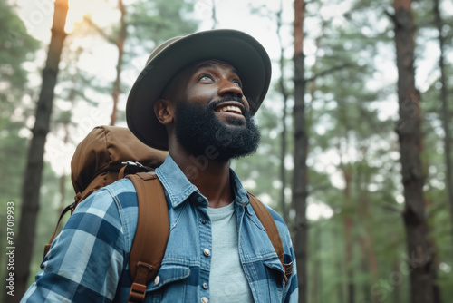 Man wearing hat and carrying backpack is pictured in peaceful forest. This image can be used to portray adventure, hiking, or nature exploration