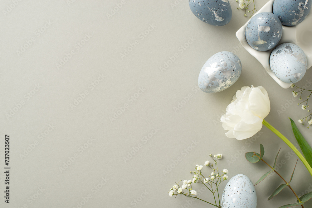 Easter aesthetic concept: Overhead view of rich greyish eggs in a special ceramic container, gypsophila, tulip, and eucalyptus arranged on a pastel grey background with space for text