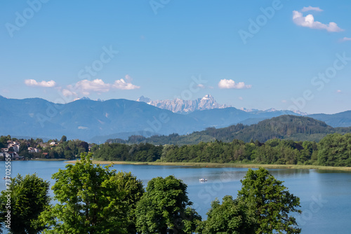 Lake Ossiach with panoramic view of untamed Julian Alps and Karawanks seen from Annenheim, Carinthia, Austria. Looking at majestic mountain peak Mangart. Wanderlust Austrian Alps in summer. Blue sky photo