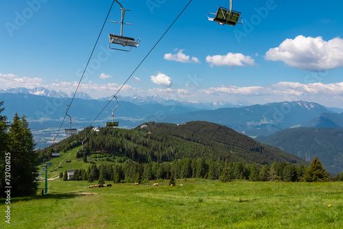 Ski lift in summer with scenic view of majestic mountain range Julian Alps seen from Gerlitzen, Carinthia, Austria. Wanderlust in Austrian Alps. Idyllic hiking trail along alpine meadow with cows photo