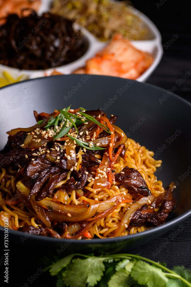 Korean food. Fried Ramen, noodles with meat and vegetables. on a black wooden background.