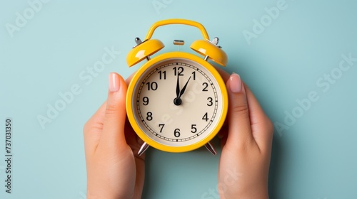 A hand holds a classic clock on a yellow base photo