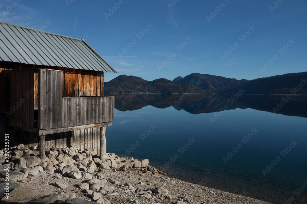 A quaint and weathered wooden shack nestled on the serene shore of a shimmering lake, offering rustic charm.