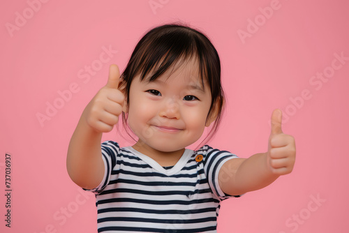 Happy little cute Asian girl giving thumbs up on pink background