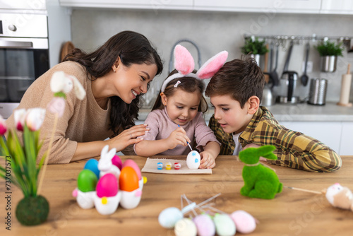 Happy easter. A mother, son and her daughter painting Easter eggs. Happy family preparing for Easter. Cute little child girl wearing bunny ears on Easter day.
