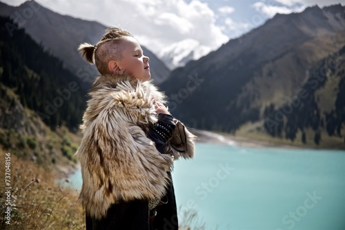 A young boy in the viking cosplay costume holding a wooden shield and a axe and standing next to the beautiful alpine lake with Mountains view photo