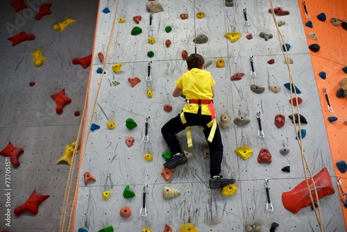 A young European boy in a yellow shirt is climbing a wall in an indoor climbing gym