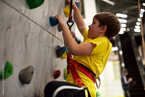 A young European boy in a yellow shirt is climbing a wall in an indoor climbing gym