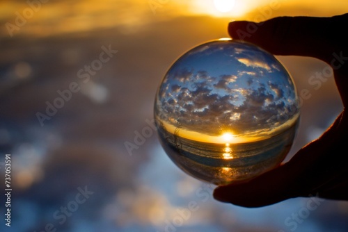 A woman s hand holds a crystal ball in which you can see a beautiful sunrise in the ocean upside down