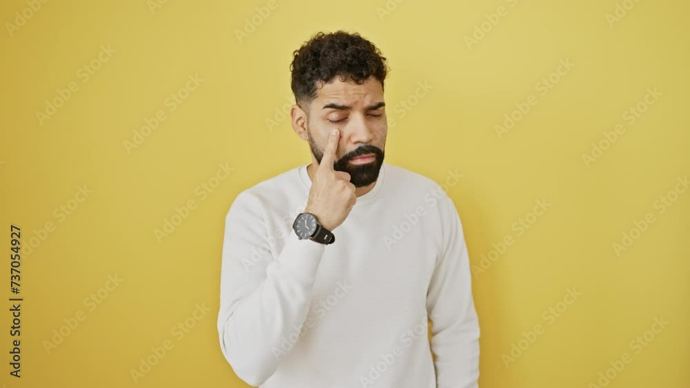 Young man's suspicious expression will get you! standing, eye-watching, finger-pointing gesture against isolated yellow background Young man's suspicious expression will get you! standing, eye-watching, finger-pointing gesture against isolated yellow background