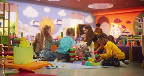Creative Multiethnic Friends Playing in Kindergarten Together with Female Pedagogue. Boys and Girls Constructing a House Out of Colorful Building Blocks. Children Having Fun in Modern Daycare Center photo